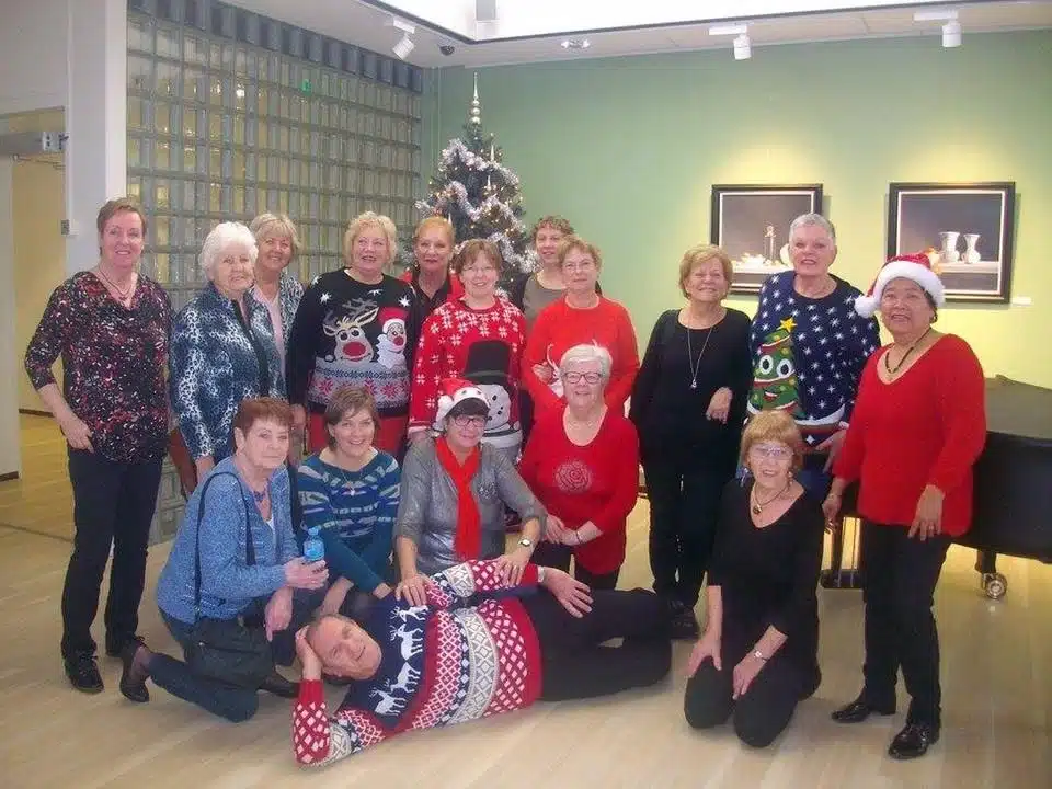 Een groep dames en man op leeftijd poseren breed lachend voor een kerstboom